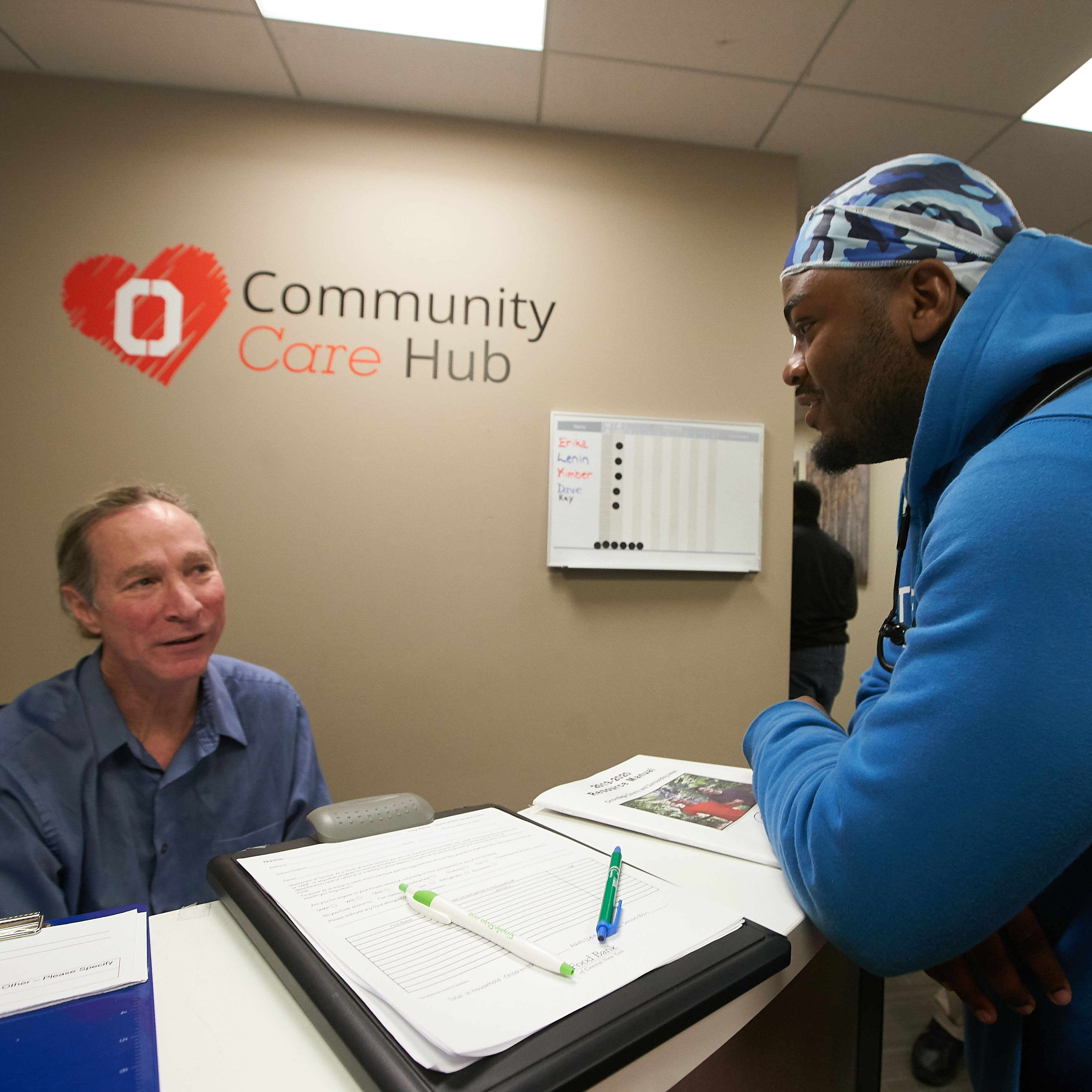 Student talking with a staff member at the Community Care Hub with the logo in the background