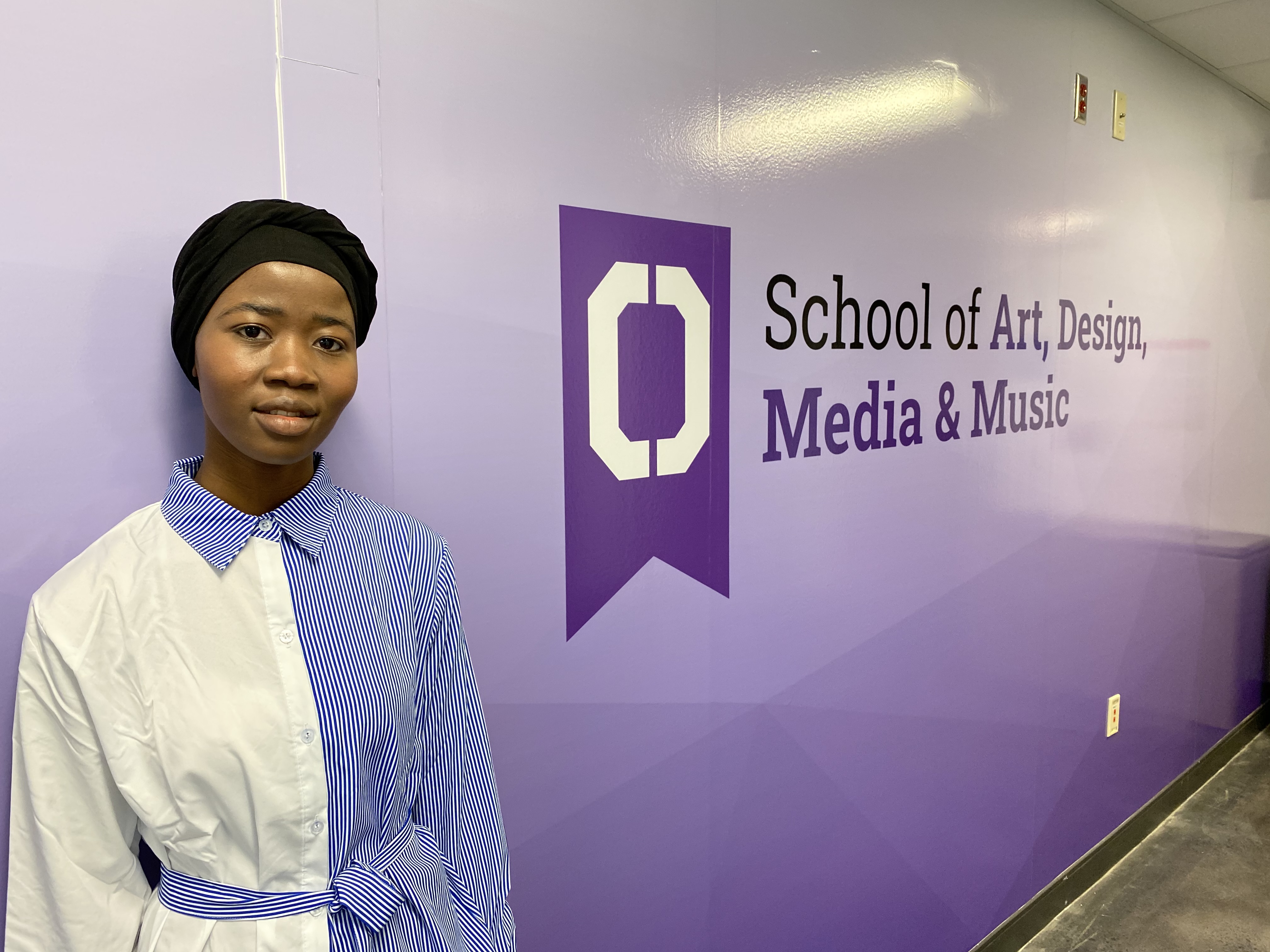 Woman standing in front of a sign that says, "School of Art, Desing, Media & Music."