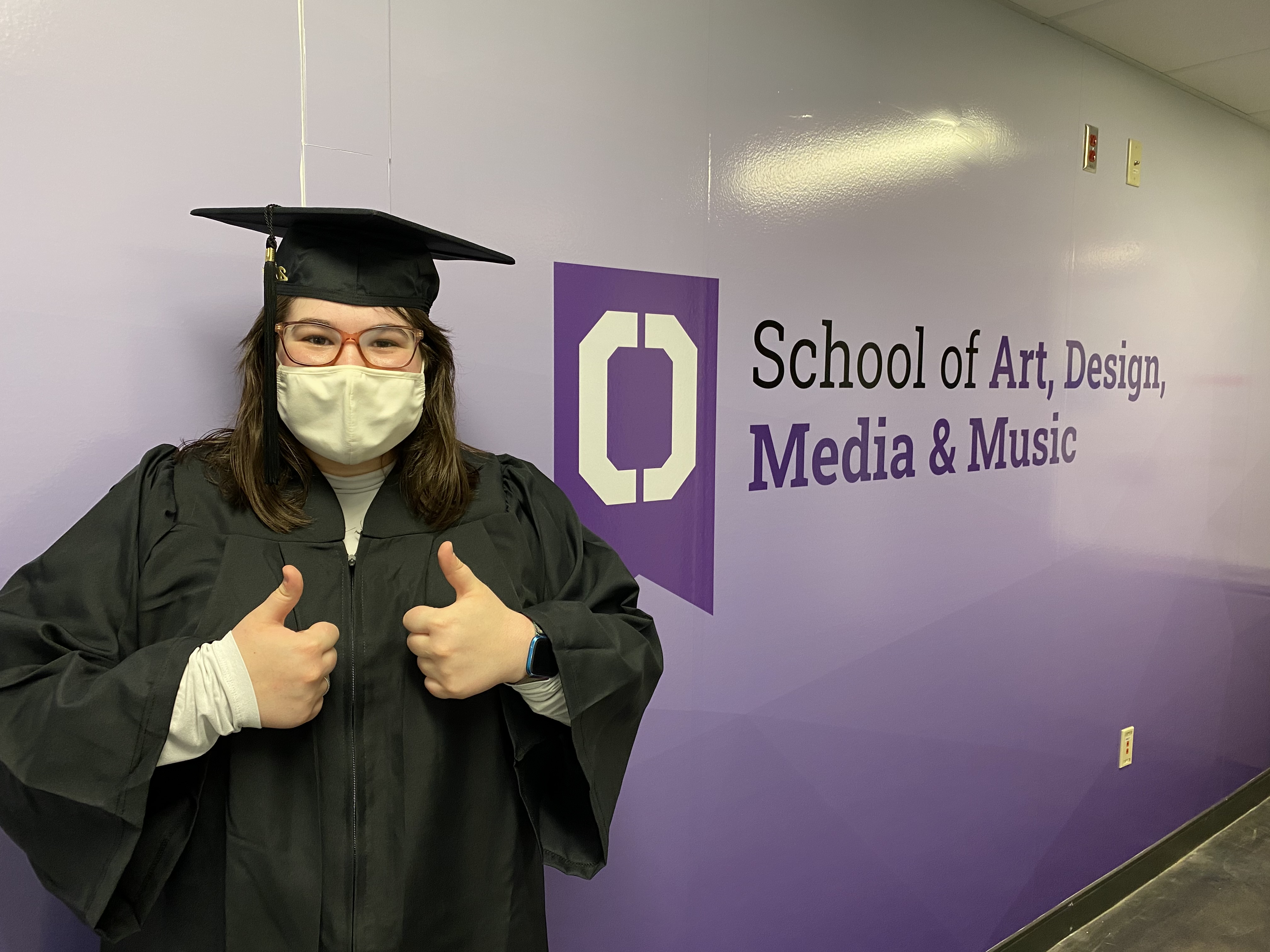 Student standing in front of a sign that says School of Art, Design, Media & Music 