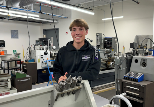 Student posing in a workshop with machinery around.
