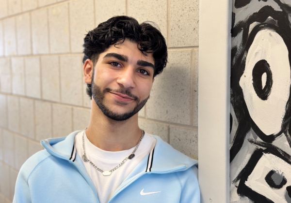 Student leaning against a wall with artwork and smiling.