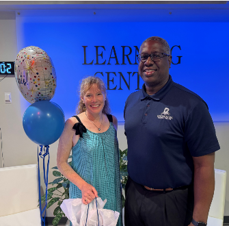 Kathleen Sisack standing next to Dr. Warren Hilton with balloons and a gift bag in the Learning Center