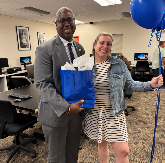 Sarah Magowan standing next to Dr. Warren Hilton with a gift bag and balloons