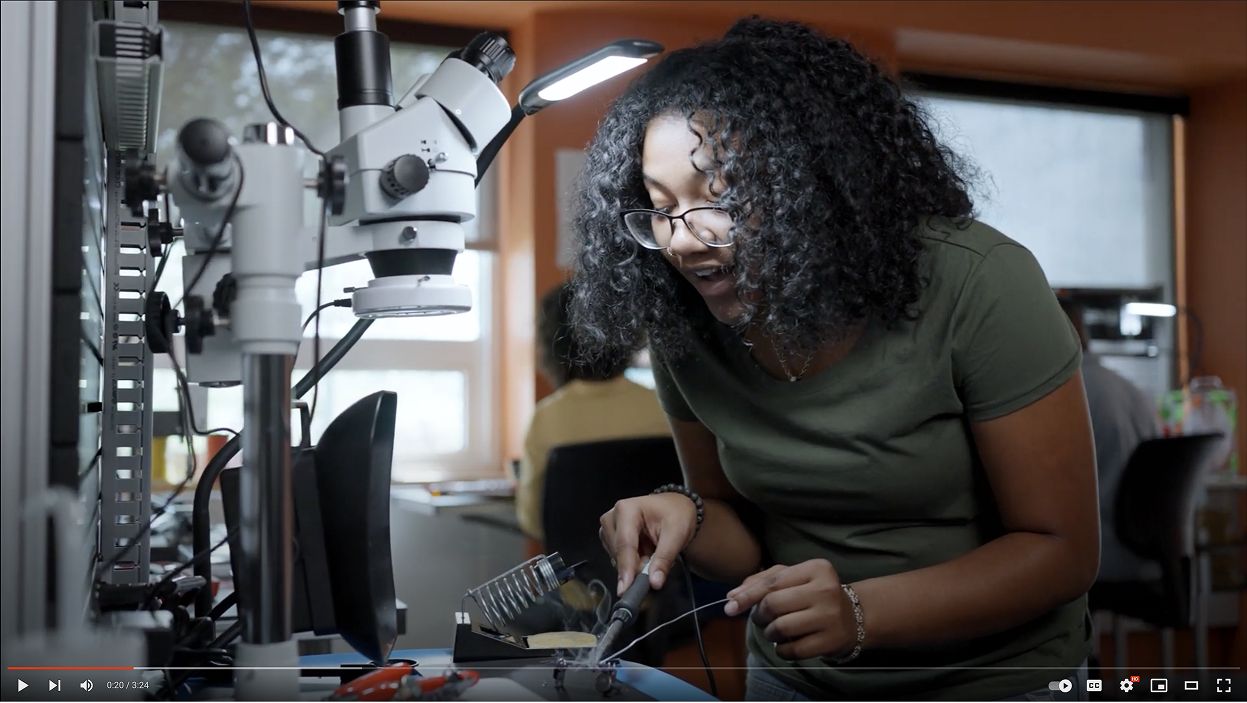 Student soldering wires at a workstation with a microscope.