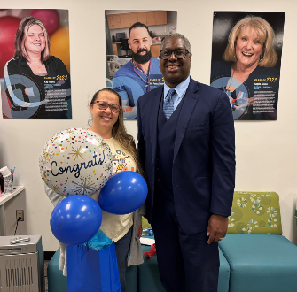 Cara Harris standing next to Dr. Warren Hilton with a gift bag and balloons