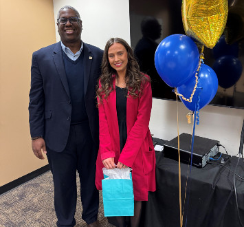Jessica Mitchell standing next to Dr. Warren Hilton with a gift bag and balloons