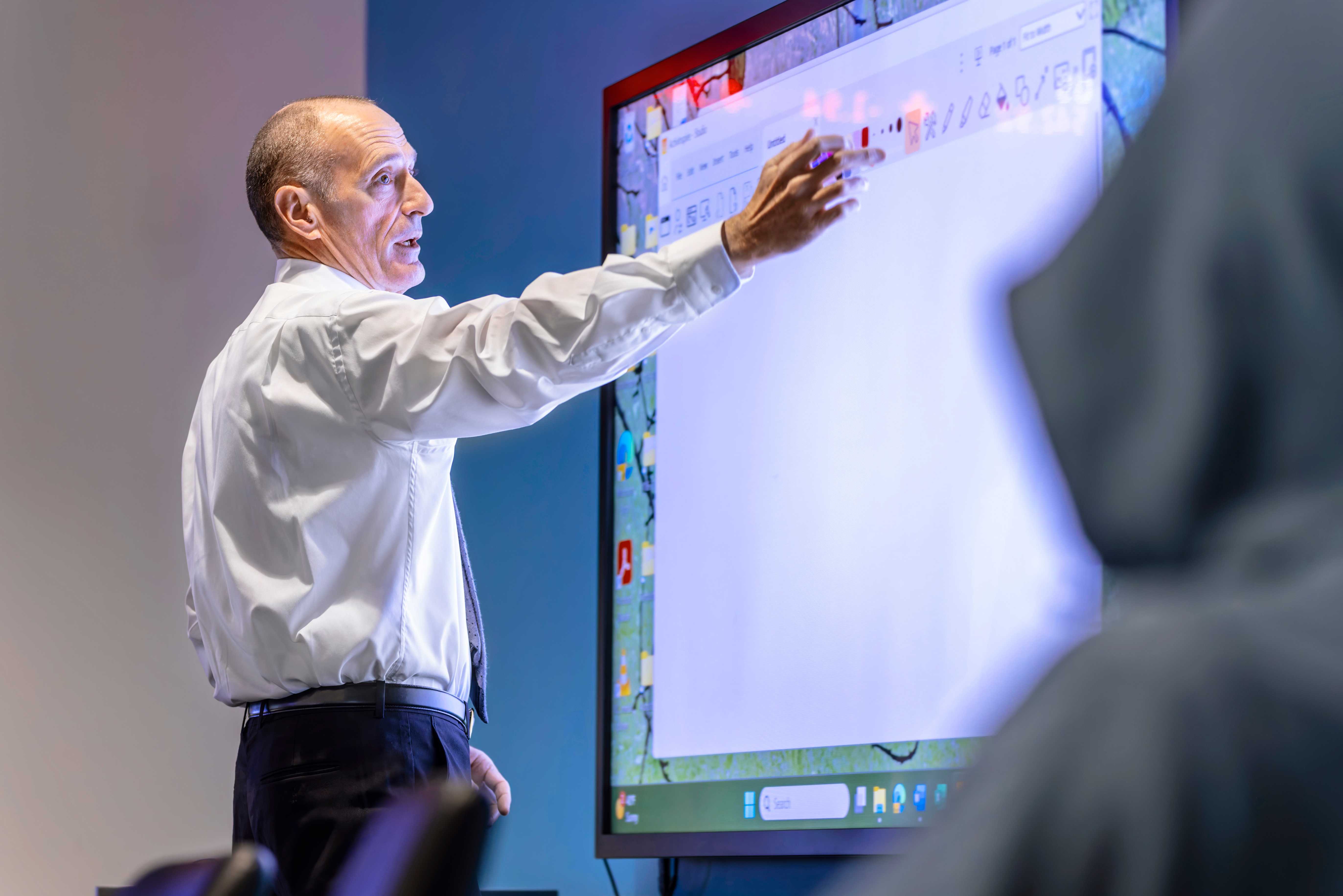 An instructor gestures at a large touchscreen display while teaching.