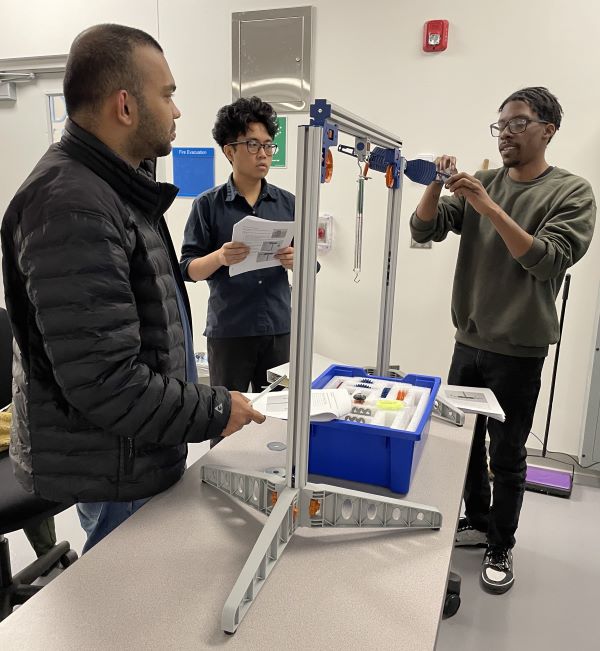 Semiconductor Bootcamp students (left to right) Sett Htun, Aaron Unger, and Brandon Simmons work together in the Basic Mechanisms module, demonstrating the concepts of levers and mechanical advantage.