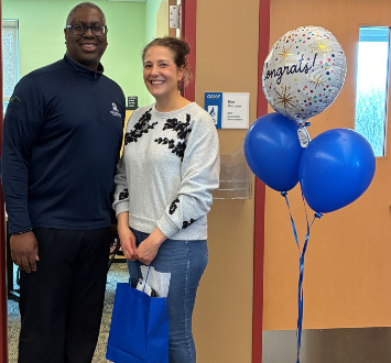 Leslie Reid standing next to Dr. Warren Hilton with a gift bag and balloons