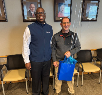 Steve Suarez standing next to Dr. Warren Hilton with a gift bag and balloons