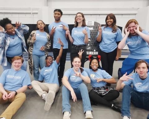 Group of smiling students in matching blue shirts posing together indoors.