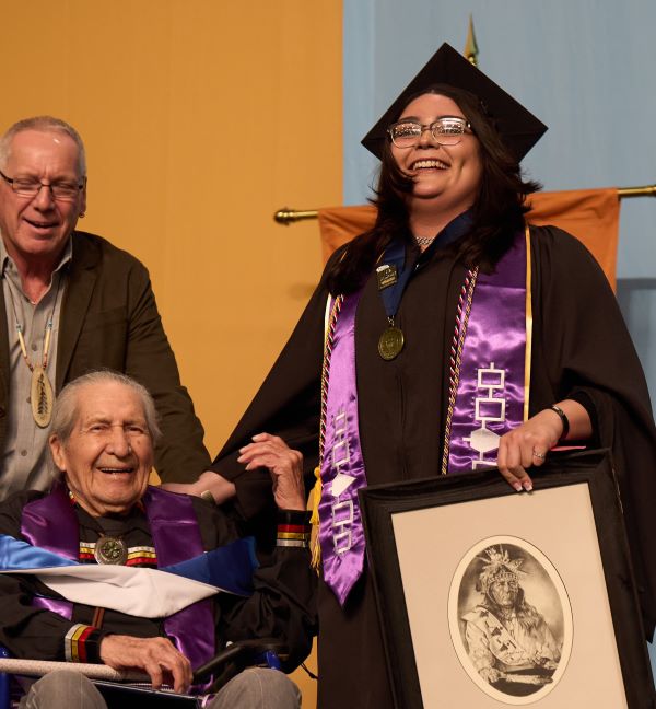 Student Speaker Kierra Yager (right) holds a drawing made by Oren Lyons (left). Behind him is Rex Lyons.
