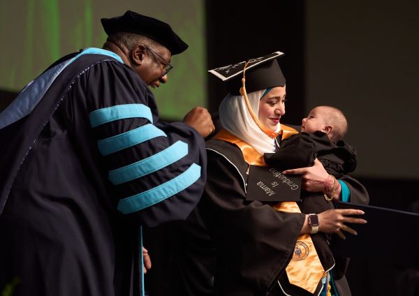 OCC President Dr. Warren Hilton (left) shared a moment on stage with a graduating student and her child.