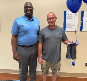Richard Bennett standing next to Dr. Hilton with balloons and a gift bag.