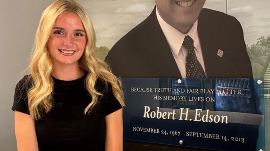 Ady Olmstead is the 2026-2027 recipient of the Robert H. Edson Memorial Scholarship. She's pictured in front of a wall honoring his legacy in the SRC Arena. Olmstead is a leader on the OCC Women's Soccer team and a Health Sciences major who plans to transfer to SUNY Upstate Medical University.