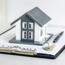 Image of a small model house with a key, pen, and contract nearby