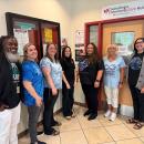 A group of six people standing in a hallway, from left to right: Jimmy Anderson, Sarah Magowan, Alex Halstead, Laura Scott, Erika Sheets, Ash Frodelius. They are standing in front of a door labeled Counseling & Community Care Hub; with various posters and signs on the wall behind them.
