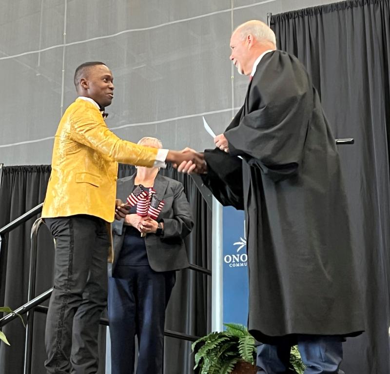 Billy Tepong Akebe (left) from Cameroon is sworn-in as an American citizen by the Honorable Glenn T. Suddaby (right). OCC President Casey Crabill (center) is also pictured. She handed American flags to each new citizen as they left the stage.