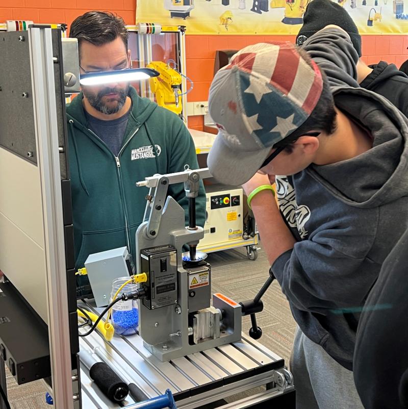OCC Professor Zachary Dineen (left) guides a Marcellus High School student as he uses an injection molding machine.
