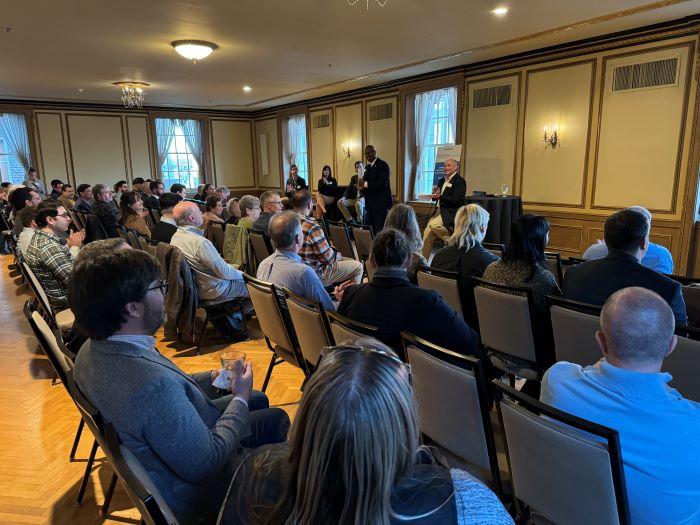 OCC President Warren Hilton (standing) speaks at the beginning of the Topics on Tap networking and panel discussion. Seated behind him (left to right) are Andrew Schuster, Lauren Staniec, Andy Breuer, and Glenn LaPoint '16.