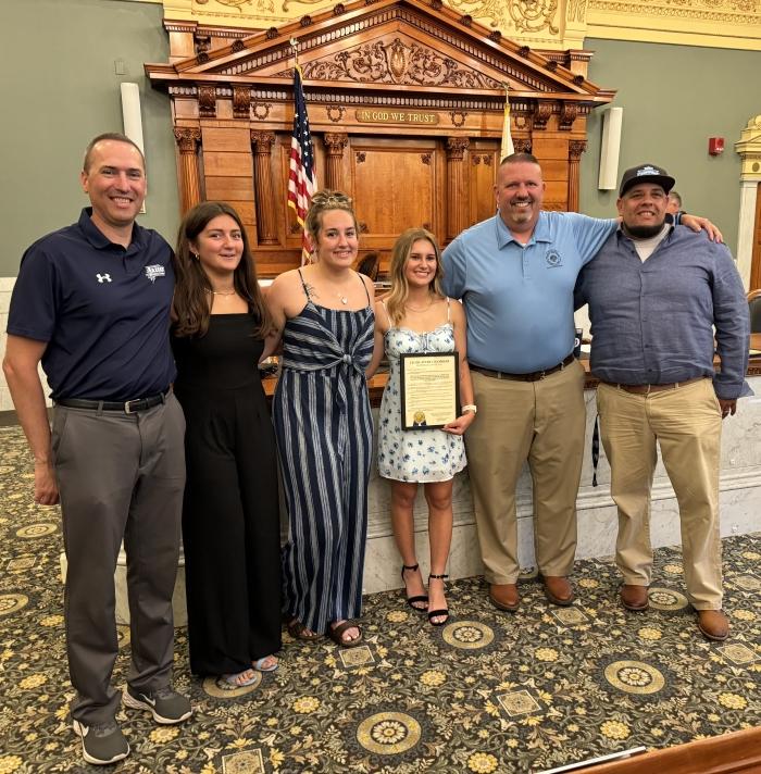 OCC's Women's Lacrosse team receives a Gold Seal Resolution at the Onondaga County Legislature. Pictured are (left to right) Athletic Director Mike Borsz, players Gianna Zerrillo, Gabriella Smart, Alecsis Buda, County Legislator Richard McCarron, and Lacrosse Head Coach Erik Mattox.