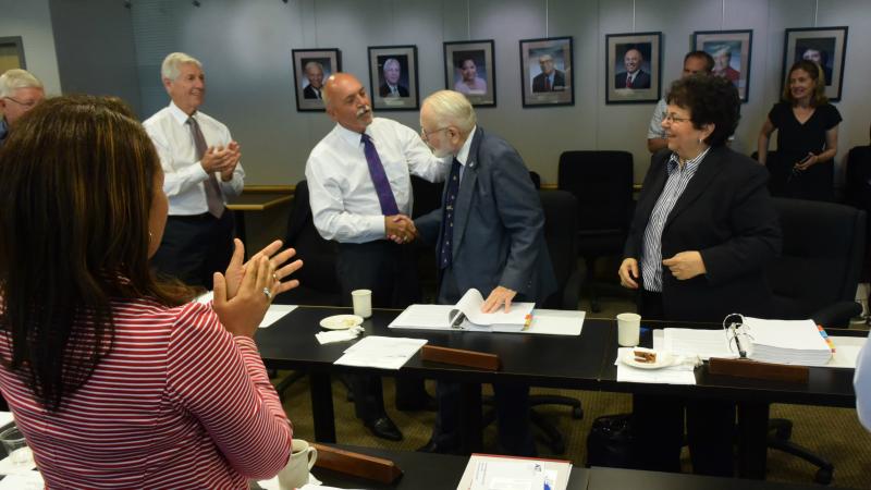 Donald Mawhinney (wearing blue blazer)  is congratulated by OCC Board of Trustees Chair Allen J. Naples and receives a standing ovation from fellow Trustees.