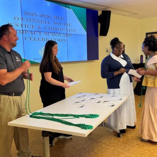 Meg O'Connell Social Justice Scholar Irielle Mwija receives her certificate and green cord. Pictured with her (left to right) are OCC's Rich Goodell, Katie Komuda, and Nira Irby.
