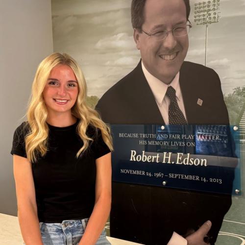 Ady Olmstead is the 2026-2027 recipient of the Robert H. Edson Memorial Scholarship. She's pictured in front of a wall honoring his legacy in the SRC Arena. Olmstead is a leader on the OCC Women's Soccer team and a Health Sciences major who plans to transfer to SUNY Upstate Medical University.