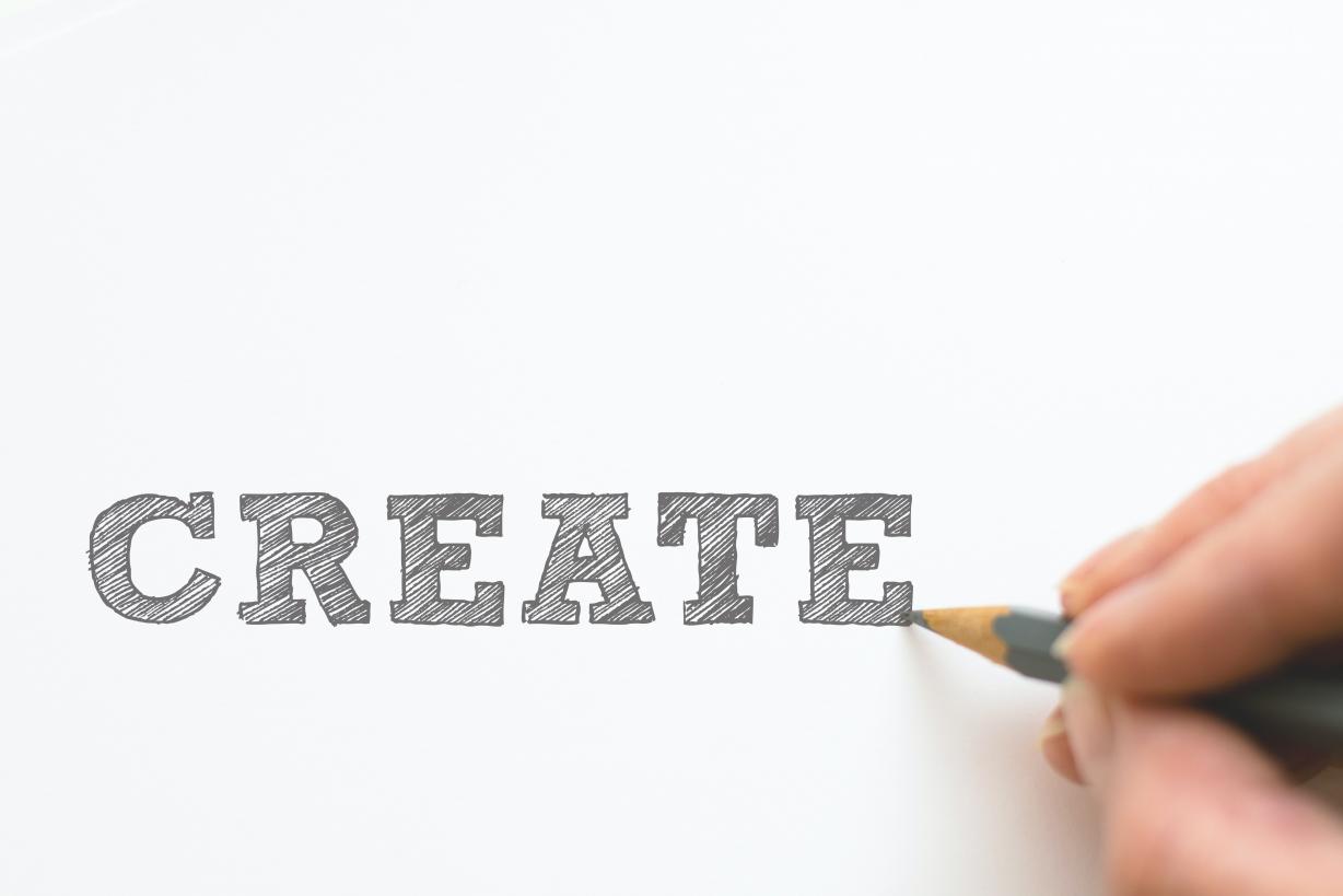 Person's hand writing the word create with a pencil 