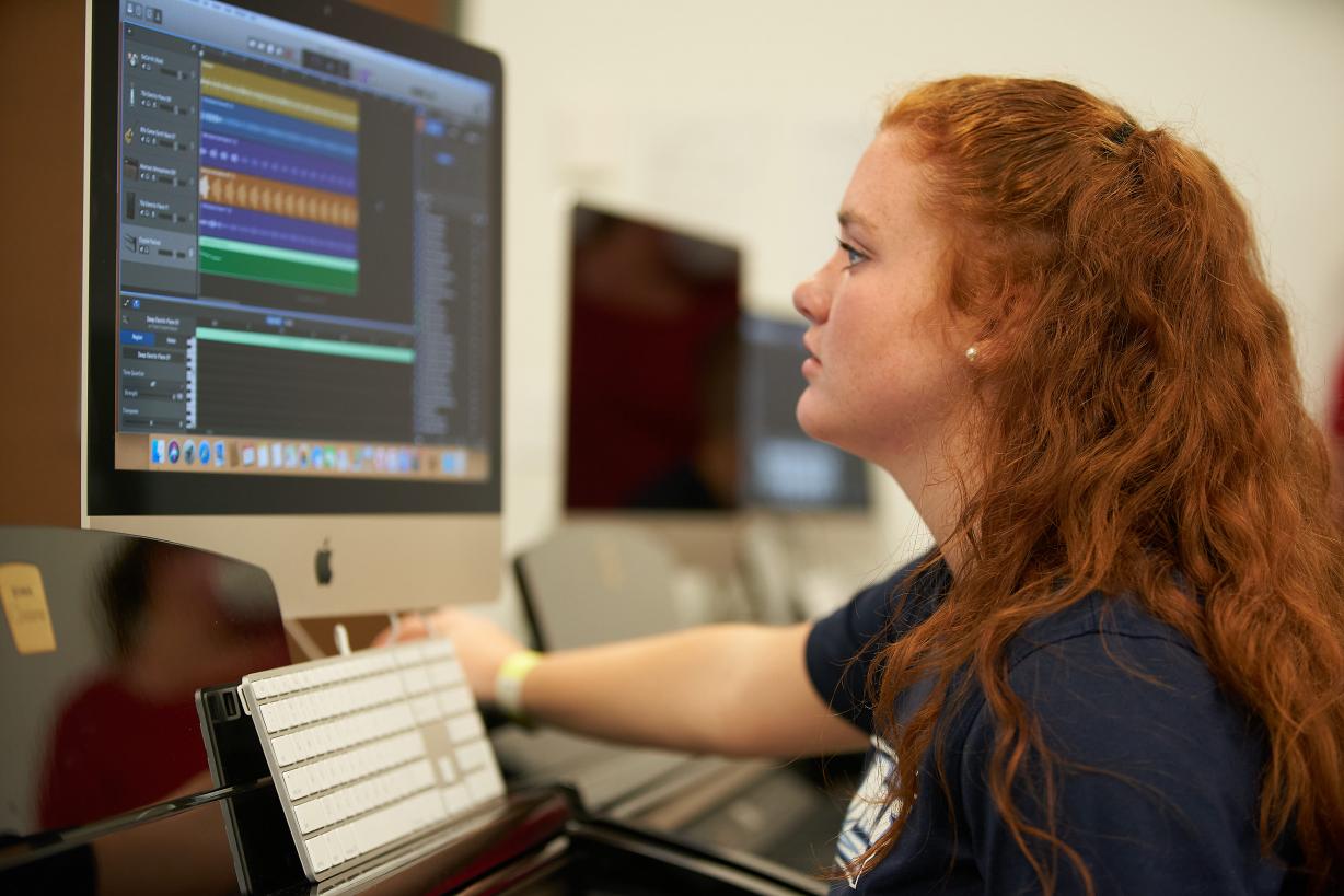 Female Student sitting at a computer with audio editing software displayed on the screen