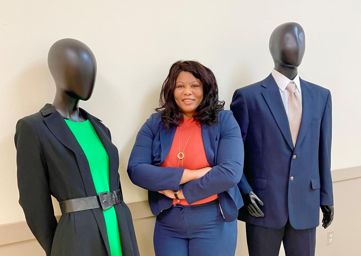 Woman of middle age in a red blouse and blue blaze standing in between and male and female mannequin in profession dress. Man is wearing a blue suite, woman is wearing a black blazer with a green dress.
