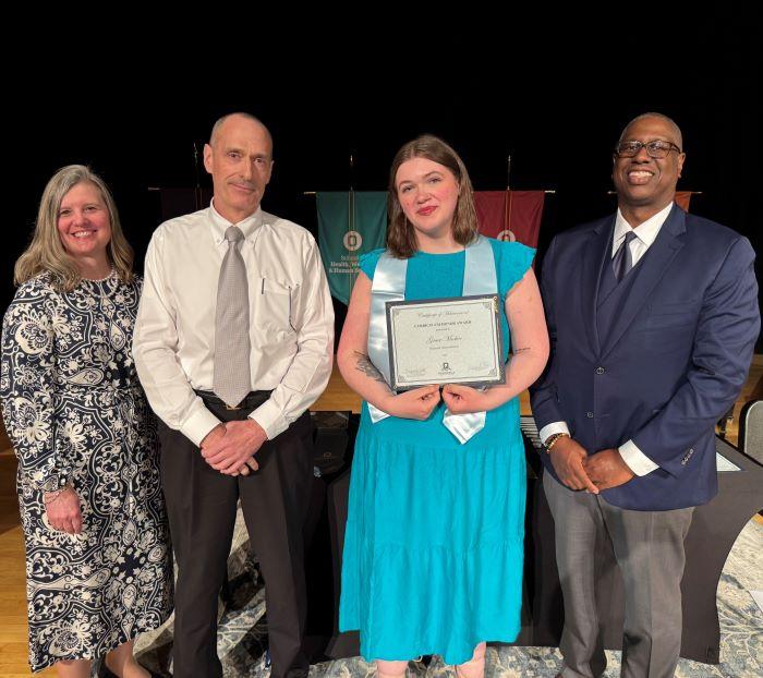 Grace Meeker (holding certificate) was named Curriculum Honoree in the Business Administration degree program. She's pictured with (left to right) Provost Anastasia Urtz, Professor JT Ryan, and President Warren Hilton.