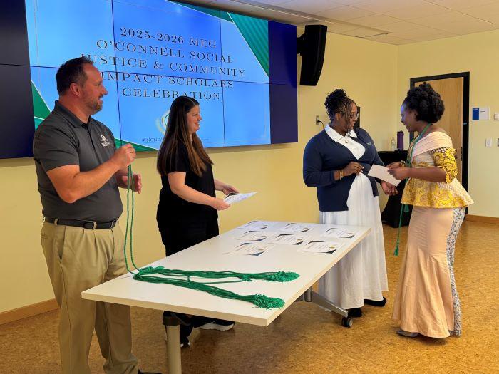 Meg O'Connell Social Justice Scholar Irielle Mwija receives her certificate and green cord. Pictured with her (left to right) are OCC's Rich Goodell, Katie Komuda, and Nira Irby.
