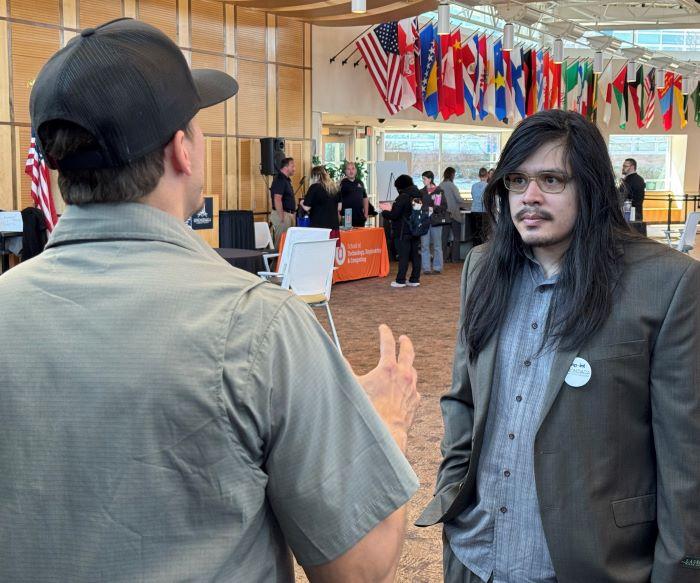 Onondaga Community College Welding major Ricky Stephens (right) speaks with a representative of Industrial Fabricating Corp at the STEM Career Showcase in the Gordon Student Center Great Room.