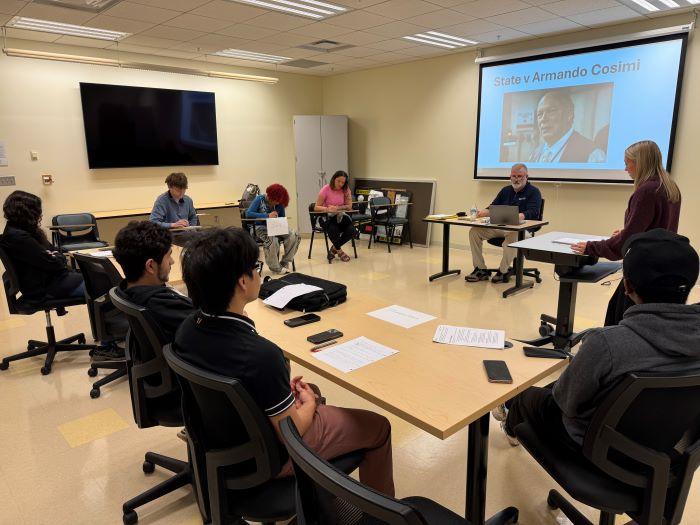 Student and prosecuting attorney Peyton George (standing, right) delivers her opening statements as part of the Criminal Investigations class final exam. Seated in front of the screen is Professor Pete Patnode who is acting as judge for the proceedings.