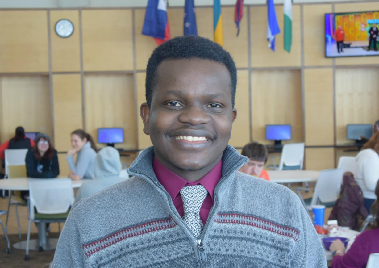 Moise Laub is pictured in the Gordon Student Center. The flag hanging closest to the clock represents his native Haiti. Laub purchased the flag and donated it to the College so it could be displayed in the Great Room.