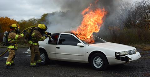 Two firemen trying to put out a car on fire 